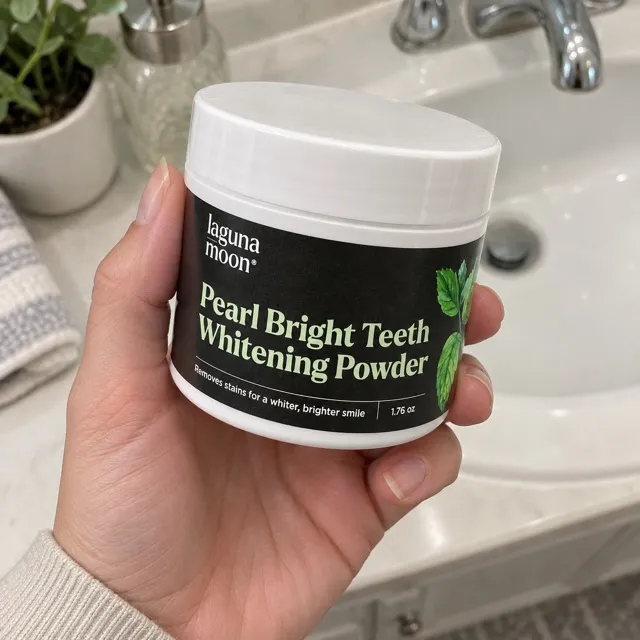 A hand holding a jar of Lagunamoon Pearl Bright Teeth Whitening Powder.